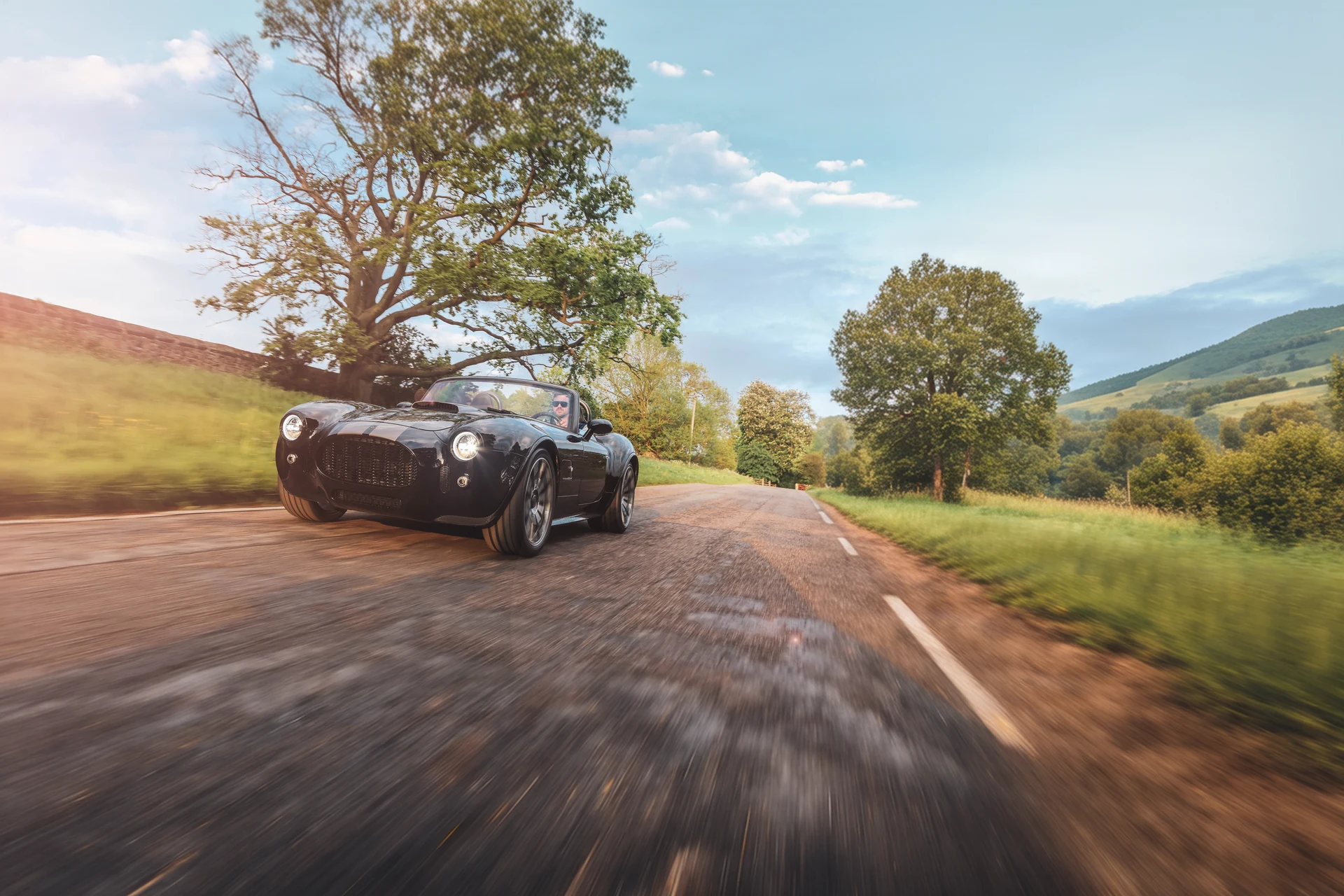 AC Cobra GT Roadster едет по загородной дороге, три четверти спереди
