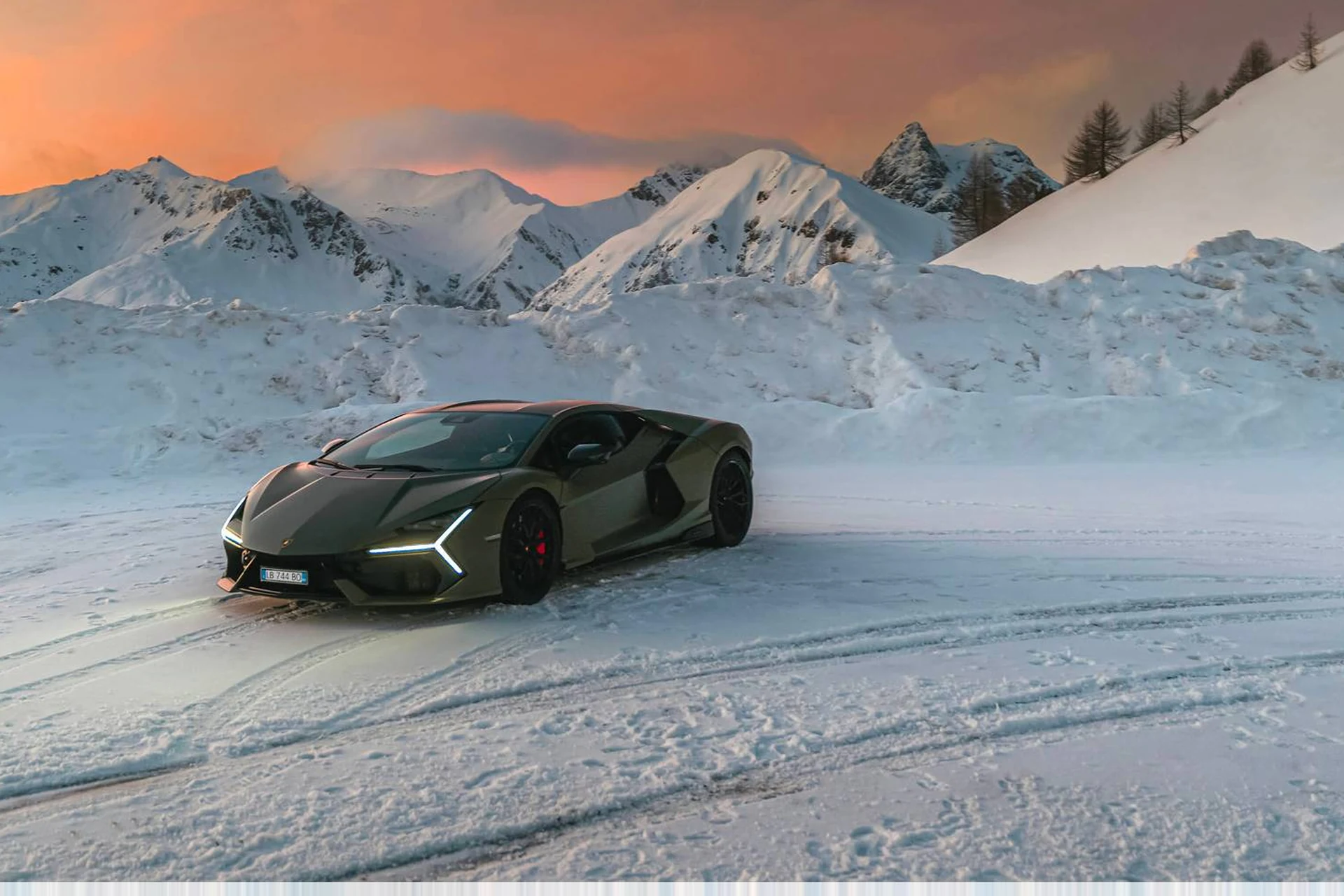 Lamborghini Revuelto на заснеженной площадке среди гор на закате, вид спереди