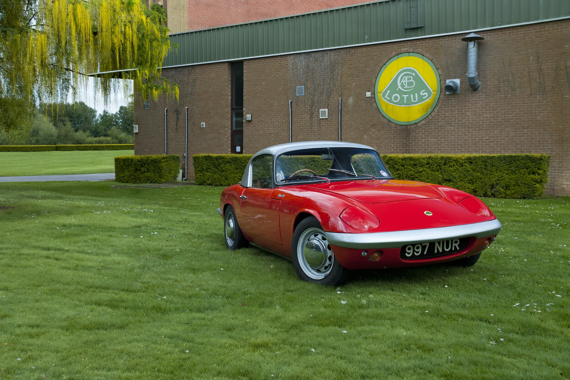 Lotus Elan 1960-х у стены завода в Хетеле со знаком Lotus
