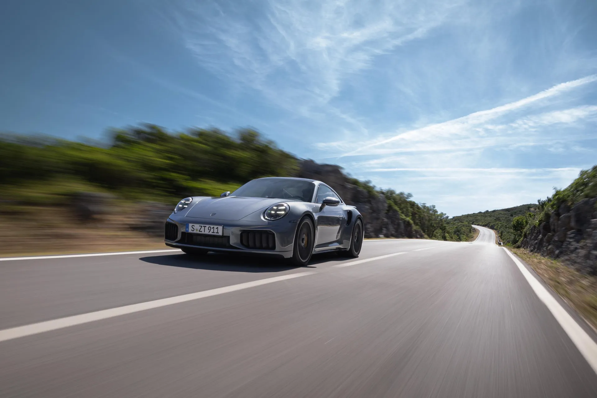 Новый Porsche 911 Turbo S в движении на горной дороге днём, вид спереди