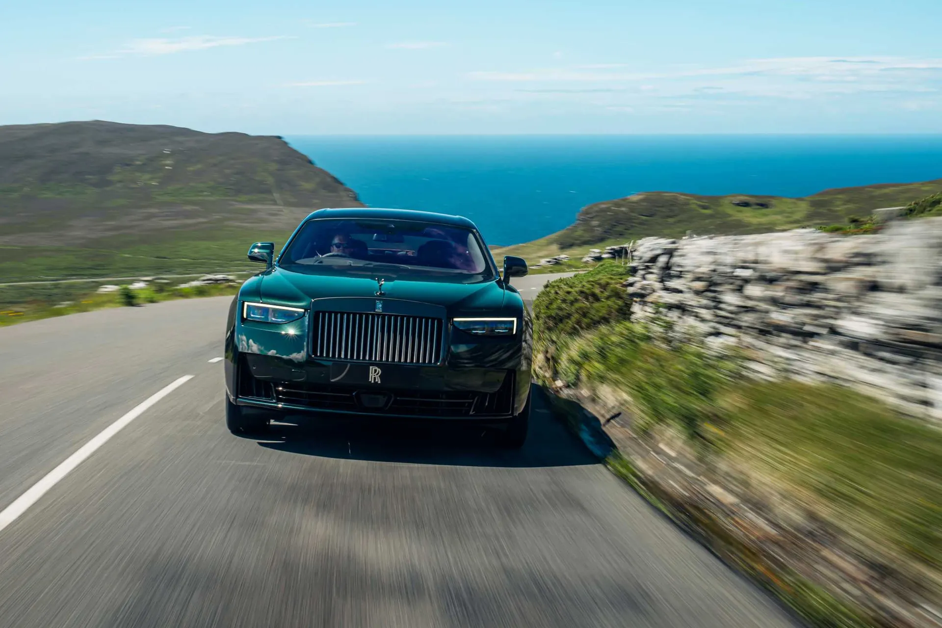 Rolls-Royce Black Badge Ghost в движении по приморской дороге днём, вид спереди